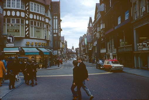 Chester, North West England, UK, 1972. Eastgate Street, Chester. Furthermore: pedestrians, shops, advertising signs, half-timbered houses and cars.