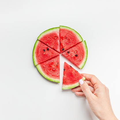 Creative scandinavian style flat lay top view of fresh watermelon slices in woman hands on white table background copy space. Minimal summer fruits creative for blog or recipe book