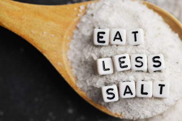 Eat less salt in order to reduce blood pressure or hypertension risk with sprinkled salt on dark background stock photo