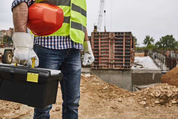 istock Ready to work! Cropped image of a builder in working uniform holding red helmet and carrying toolbox while standing at construction site 1142819007