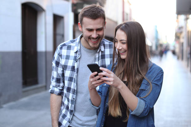 istock Happy couple walking using cell phone in the street 1142820469