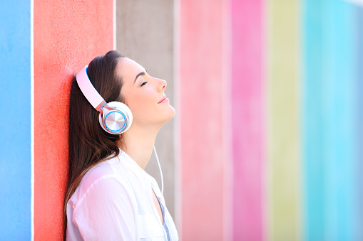 Relaxed girl listens to music leaning in a colorful wall