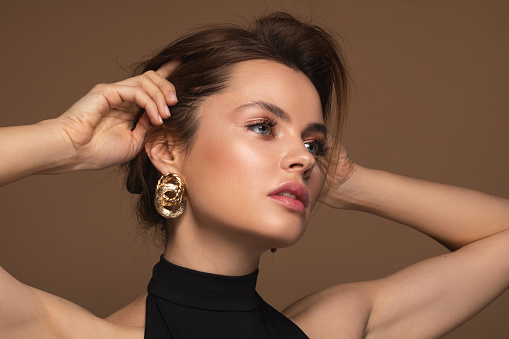 Portrait of a gorgeous woman with makeup and golden earrings thoughtfully looking away and touching her hair
