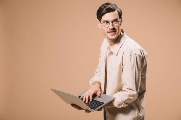 istock cheerful man in glasses using laptop isolated on beige 1142826826