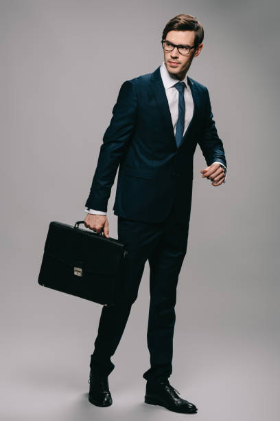 istock serious businessman in suit holding briefcase on grey background 1142827841