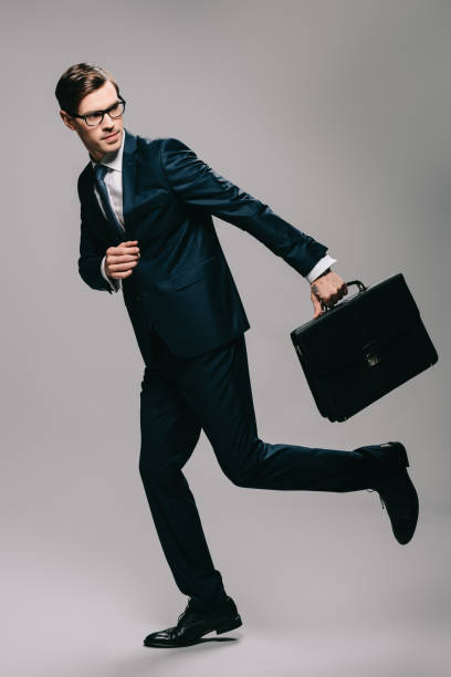 istock confident businessman in suit running with briefcase on grey background 1142827853