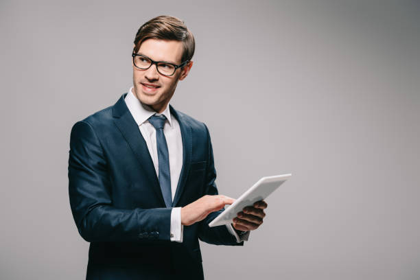 istock cheerful businessman in glasses using digital tablet isolated on grey 1142827876
