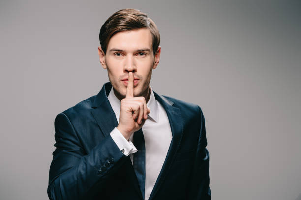istock handsome businessman putting finger on lips on grey background 1142827940