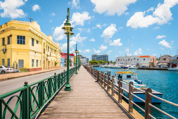 Promenade at marina of Bridgetown, Barbados. Bright image of wooden promenade at the waterfront of Bridgetown in Barbados. Colorful building against blue sky with white clouds. Boats and yachts in the harbor. barbados stock pictures, royalty-free photos & images