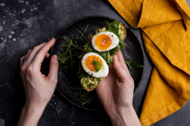 Toast with egg and avocado on bread in woman's hands on black background Toast with egg and avocado on bread in women's hands on black background. Top view, table top, flat lay. Concept of healthy breakfast. Lifestyle photography boiled stock pictures, royalty-free photos & images