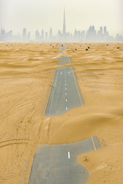 vista desde arriba, impresionante vista aérea de una carretera desierta cubierta por dunas de arena en el medio del desierto de dubái. hermoso horizonte de dubái rodeado de niebla en el fondo. dubai, emiratos árabes unidos. - desert road road urban road desert fotografías e imágenes de stock