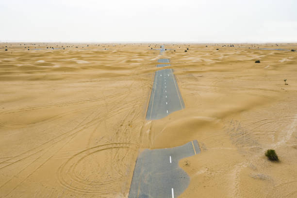 blick von oben, atemberaubende aussicht auf eine menschenleere straße, die von sanddünen mitten in der wüste von dubai bedeckt ist. dubai, vereinigte arabische emirate. - fog desert arabia sunset stock-fotos und bilder