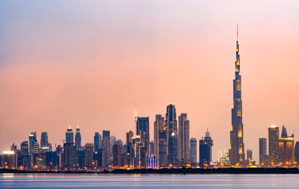 Stunning panoramic view of the illuminated Dubai skyline during sunset with beautiful shades of pink and orange colors. Silky smooth water flowing in the foreground. Dubai, United Arab Emirates. Stunning panoramic view of the illuminated Dubai skyline during sunset with beautiful shades of pink and orange colors. Silky smooth water flowing in the foreground. Dubai, United Arab Emirates. dubai skyline stock pictures, royalty-free photos & images