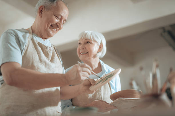 istock Low angle of smiling elderly craftsman painting decorative plate in workshop 1142834344