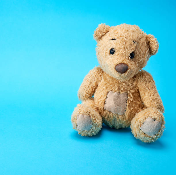 istock very old brown teddy bear on a blue  background 1142836474