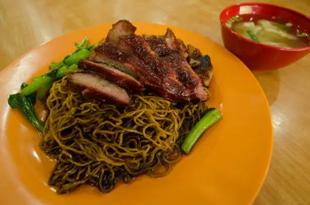 Photo of Close-up view of the wantan mee served with soy sauce,roast pork and vegetable. It is a Cantonese Chinese cuisine.