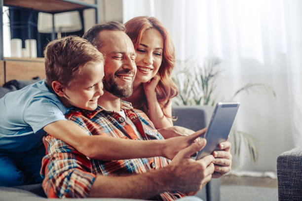 Wonderful weekend at home with your family Waist up photo of smiling parents and child watching new game on tablet while sitting on sofa. Copy space on right side desire photos stock pictures, royalty-free photos & images