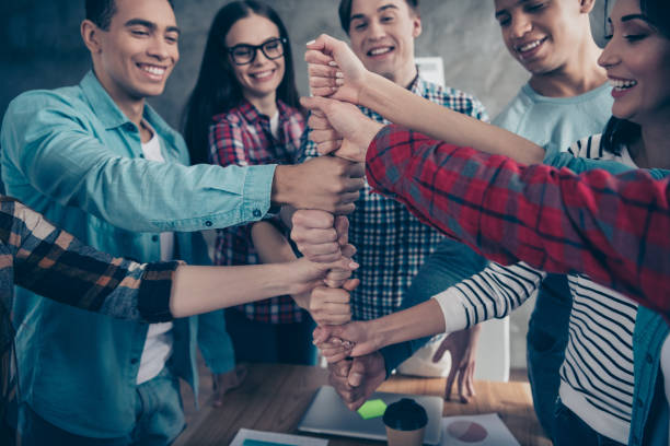 istock Optimistic positive joyful unity of college students girl guys race having doing coaching exercises happy smile wear casual shirts situated in modern office placing fists together 1142840013