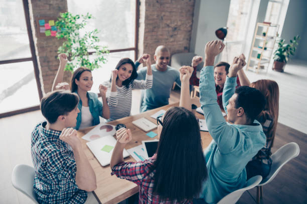 istock Excited delighted managers partners professionals champions after brainstorming having training seminars aims gesturing raising fists sitting at desk office 1142840116