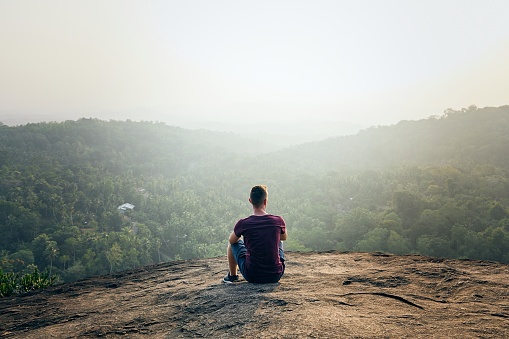 Young man resting on top of rock. Landscape at foggy sunset in Sri Lanka.