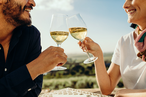 Cropped shot of a couple sitting together with glasses of white wine on a wine date. Side view of a couple on a date talking to each other toasting glass of wine.