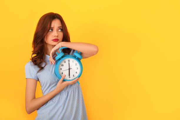 istock Young woman studio isolated on yellow holding alarm clock concerned 1142850902