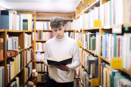 Young male student reading a book in a library.