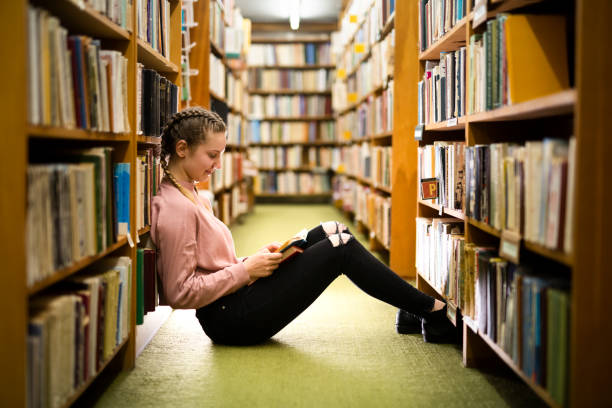 istock Female student sitting on library floor at college campus 1142852553