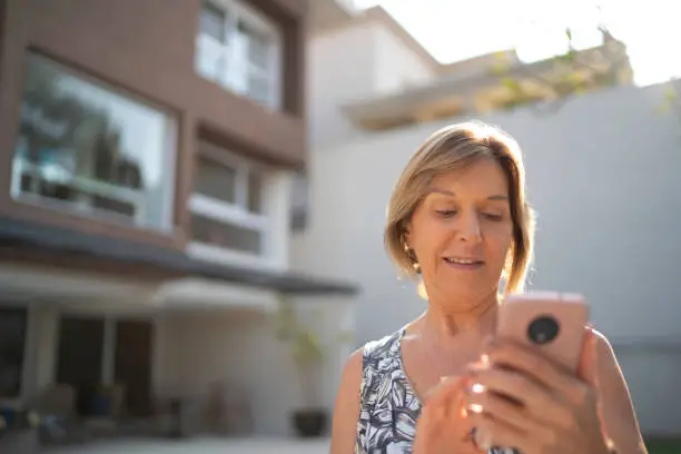 Mature woman in front of a house using mobile