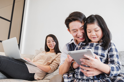 Happy Asian family spending time together at home playing game, tablet for education