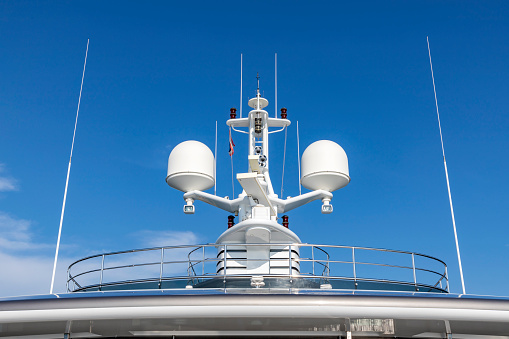 Communication antennas with navigation equipment, radar on the upper deck of the luxury white cruise ship.  There is a Thai flag with clear blue sky in the sunny day.