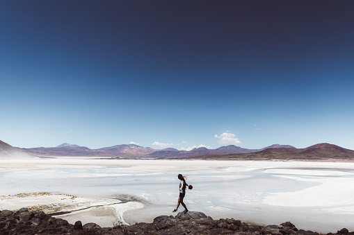 Silhouette of woman walking at scenic big salt flat and looking at colorful mountains in Atacama region, Chile
