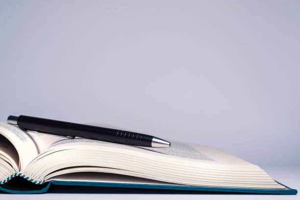 un libro a copertina rigida semiaprito con un'elegante penna nera a sfera appoggiata sulle pagine gialle - open book teaching table foto e immagini stock
