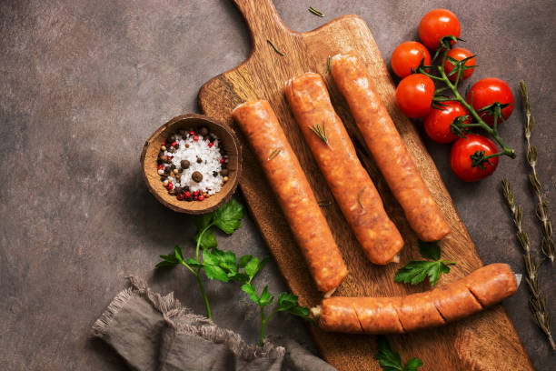 istock Raw sausages with cherry tomatoes and spices on a cutting board, rustic brown background. Top view, flat lay,copy space 1142866414