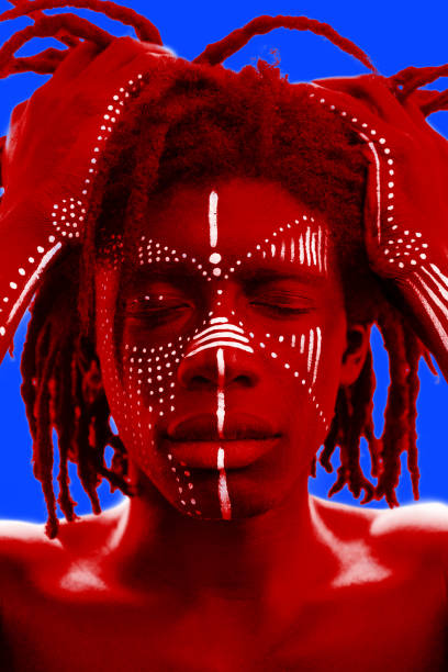 Portrait photography plays with color contrasts un llamativo macho de piel oscura muestra patrones pintados de cara blanca tradicionales que contrastan su piel retrato de un hombre de piel oscura con rastas y pintura facial tribal sostiene el pelo con las manos. tonalidad roja sobre fondo azul.