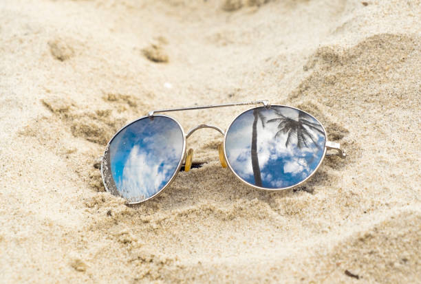 istock Mirrored sunglasses close up on the beach sand with palm trees reflection 1142870998