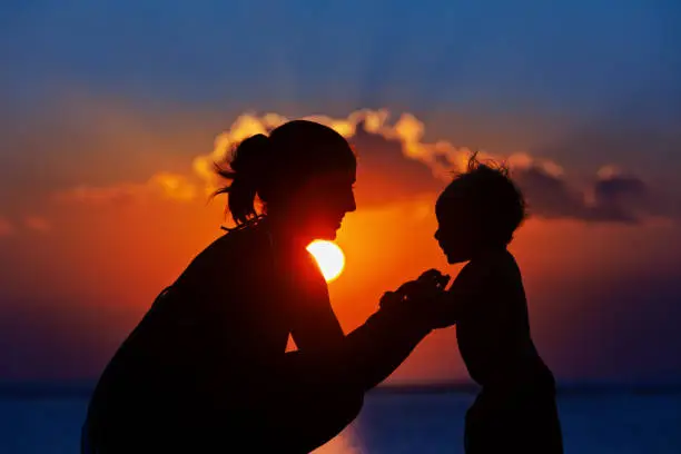 Photo of Black silhouette of mother, baby son walk by sea beach