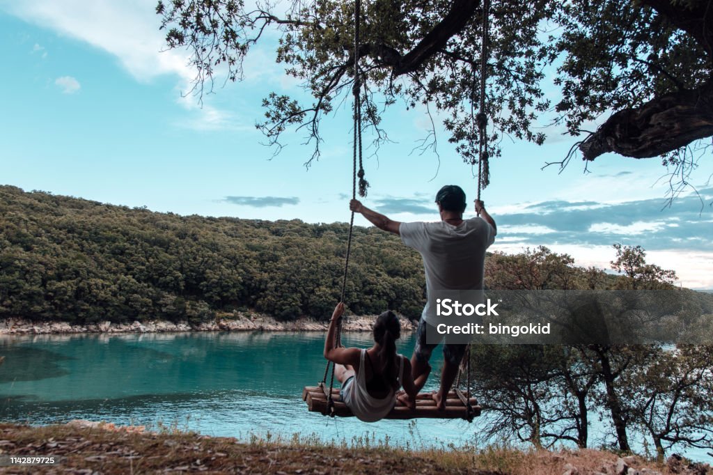 Young couple on a swing by the sea Using A Swing Stock Photo