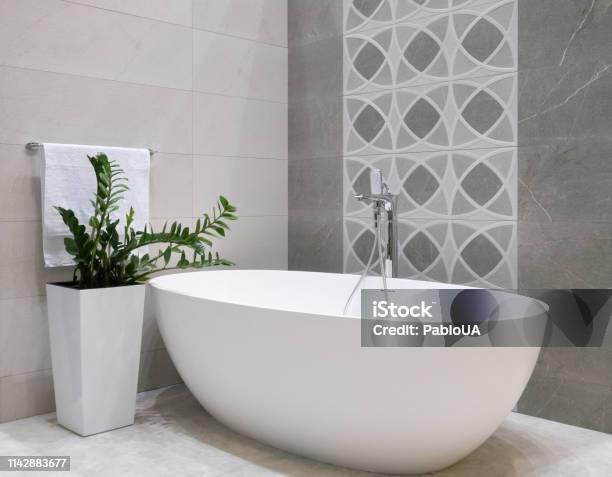 Modern Bathroom Interior Design With White Stone Bathtub Grey Tiles Wall Ceramic Flowerpot With Green Plant And Hanger With Towel Stock Photo - Download Image Now