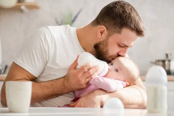 Photo of Young father kiss his baby during drinking milk
