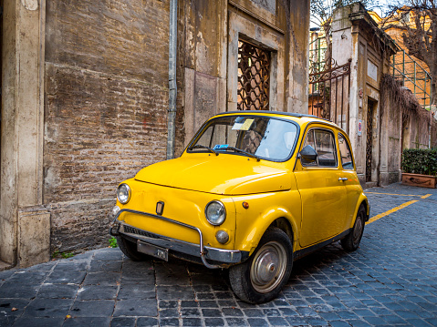 A vintage yellow Fiat 500 parked along a stone alley in the Piazza di Spagna district in the heart of Rome