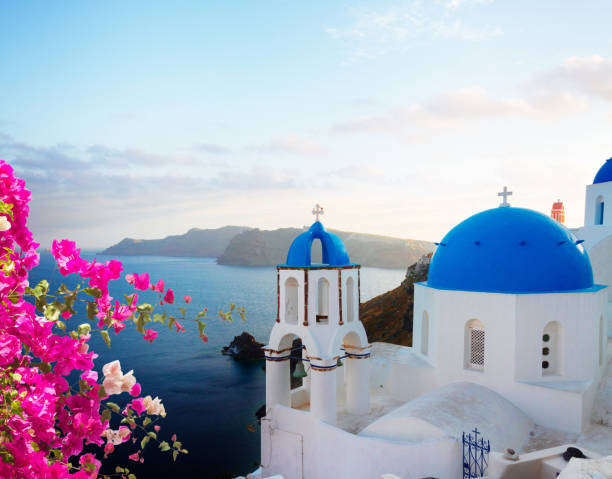 traditional greek village Oia of Santorini, with blue domes of churches in sunset light with flowers, Greece