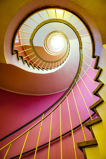 Color image depicting an abstract high angle view of a concrete spiral staircase. We can see the blurred motion of a group of people walking up and down the staircase, giving the impression that they are moving fast.  Room for copy space. ***image taken in City Hall, London, UK, a publicly owned building freely accessible to the public without entry fees or photographic restrictions***