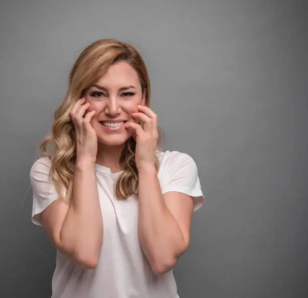 Panic attack. A young woman holds her forehead with her hands and screams. On a gray background.