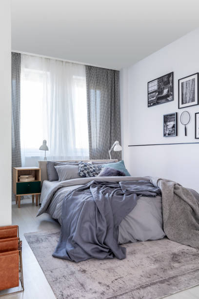 istock Grey sheets on bed and patterned drapes at window in bedroom interior with posters. Real photo 1142892715