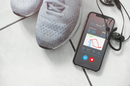 Mobile phone and headphones resting against a pair of trainers. The screen is displaying a fitness app showing the users run details.