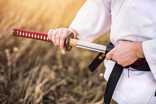 Hand close-up of martial artist holding his katana while practicing in nature.