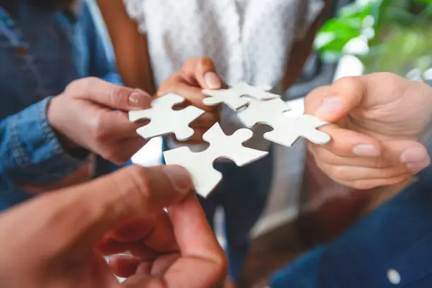Group of business people holding a jigsaw puzzle pieces. Jigsaw pieces fit into each other. Business solution integration concept. Multi ethnic group. Close up of hands