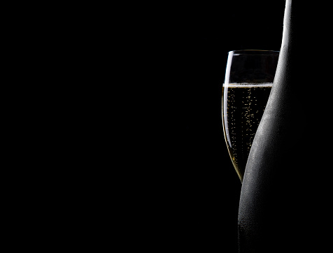 Glass and bottle of champagne on a black backround. There are bubbles in the champagne glass. Copy space