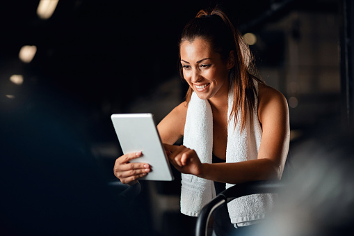 Happy sportswoman making her exercise plan on digital tablet while having sports training in fitness center.